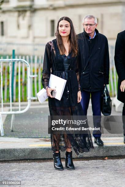 Guest wears a black lace mesh dress, holds a telephone, has black shoes, outside Chanel, during Paris Fashion Week -Haute Couture Spring/Summer 2018,...