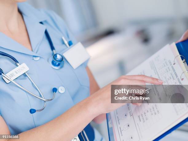 nurse looking at patientõs medical chart - medisch dossier stockfoto's en -beelden