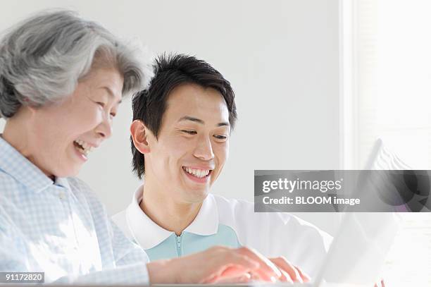 senior woman and male care worker using laptop pc - 介護施設 ストックフォトと画像