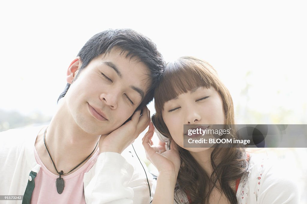 Young couple listening to music with headphones, with eyes closed