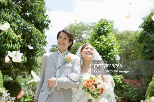 bride and groom in flower shower, smiling, walking arm in arm - trauung stock-fotos und bilder