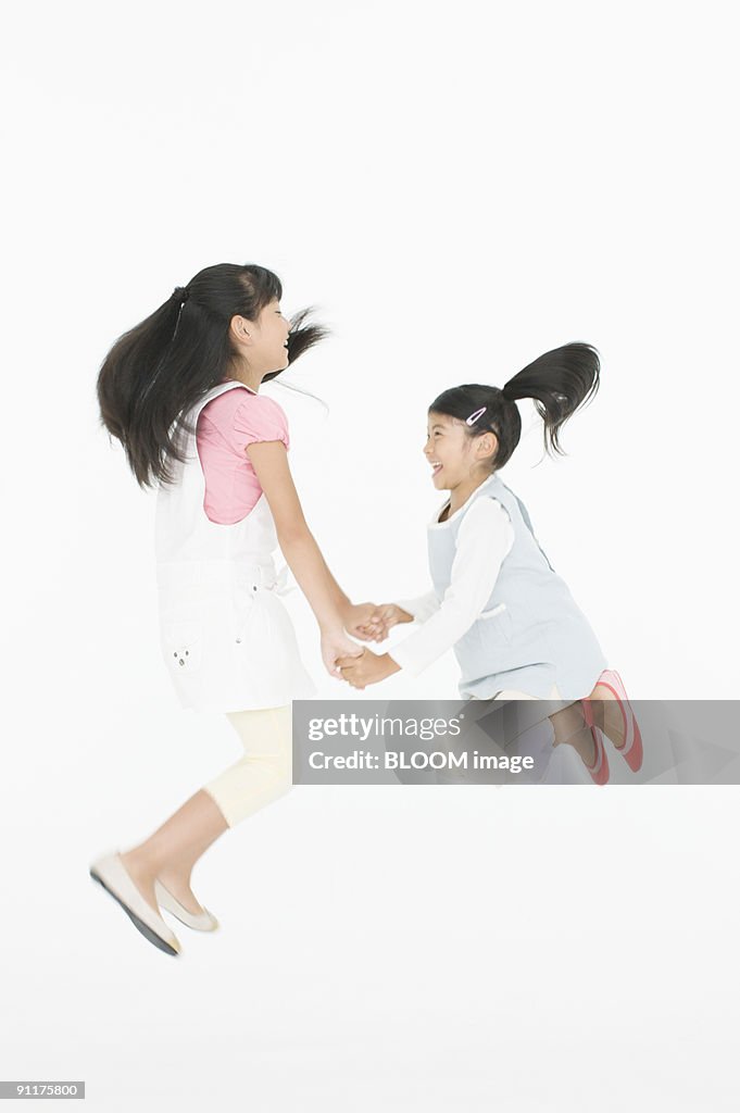 Girls jumping, holding hands, studio shot