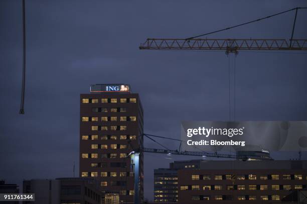 Construction cranes stand before sunrise as the ING Groep NV logo sits illuminated on top of the lender's Acanthus headquarter building complex in...