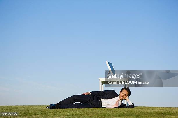 businessman lying by desk in field - lying on side stockfoto's en -beelden