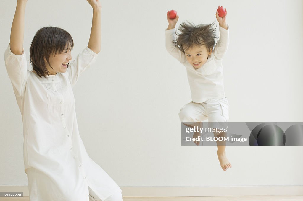 Mother smiling at son jumping and holding apples
