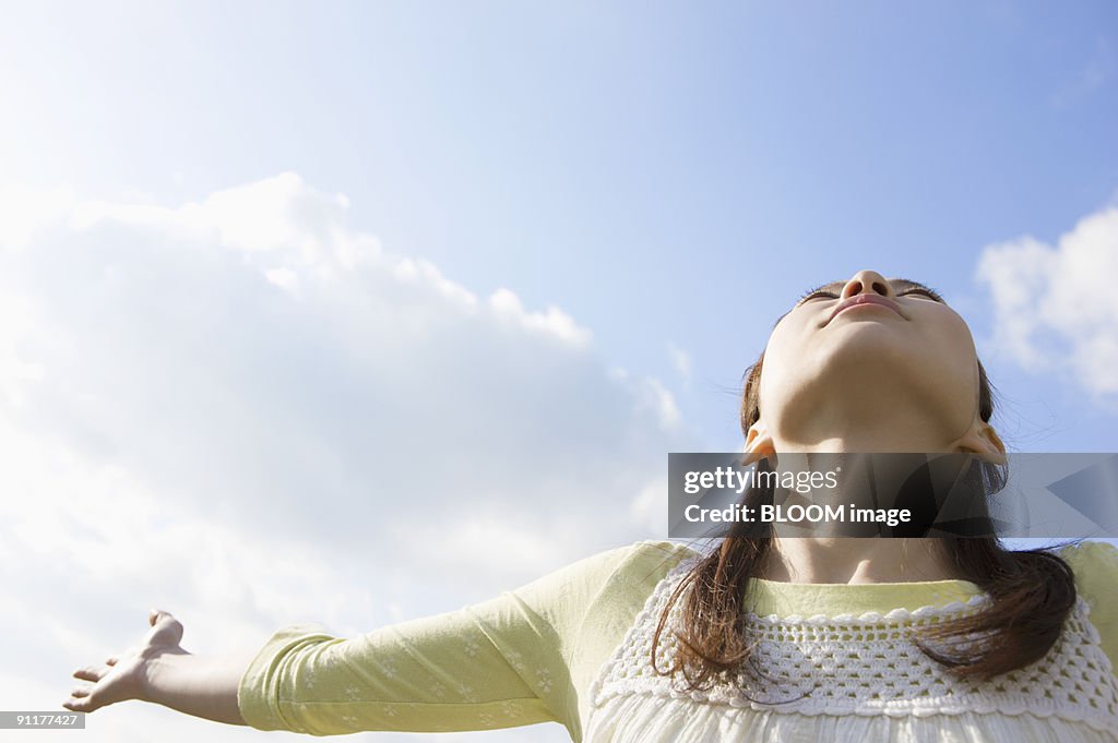 Young woman stretching arms against sky