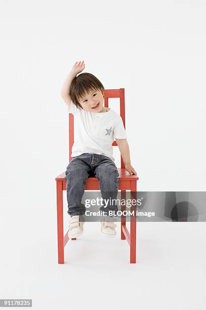 boy raising hand sitting on chair, studio shot - 2 jeunes timide fond blanc photos et images de collection