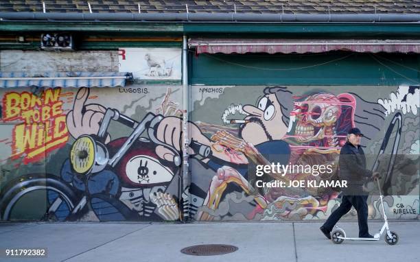 Man pushes his scooter by a graffiti at Naschmarkt market in Vienna, Austria on January 29, 2018. / AFP PHOTO / JOE KLAMAR