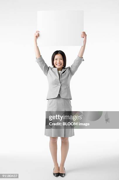 businesswoman holding whiteboard over head, studio shot - 腕を上げる ストックフォトと画像