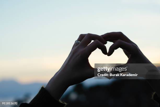 hand shaped heart against sunset - liebe auf den ersten blick stock-fotos und bilder