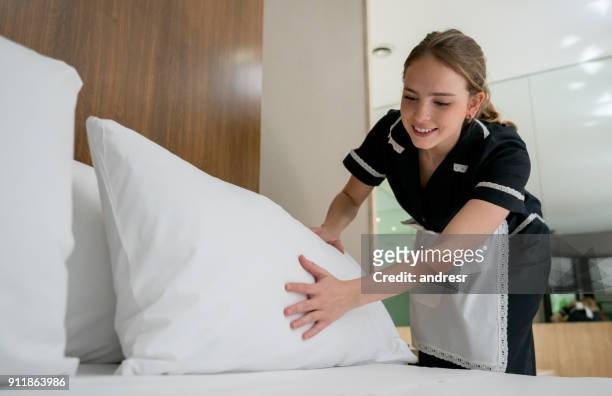 housekeeper making the bed at a hotel looking happy - hotel stock pictures, royalty-free photos & images