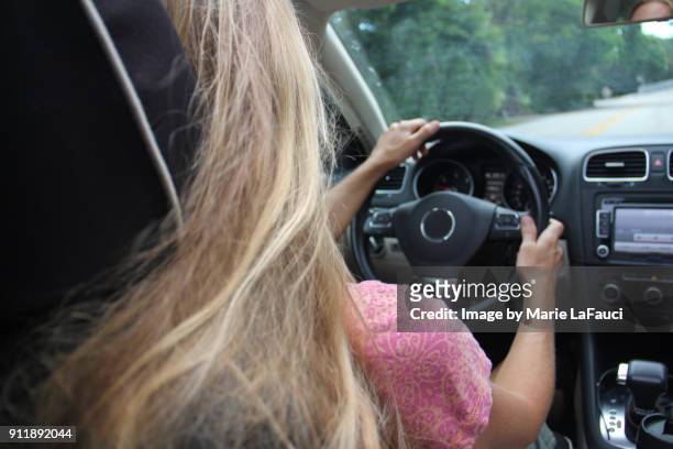 rear view of woman driving in car with two hands on the wheel - passenger seat foto e immagini stock