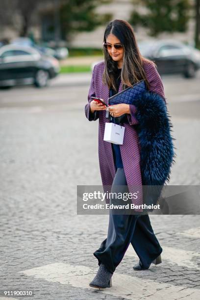 Guest wears a purple coat, a fur scarf, a chanel bag, wide pants, holds a smartphone, outside Chanel, during Paris Fashion Week -Haute Couture...