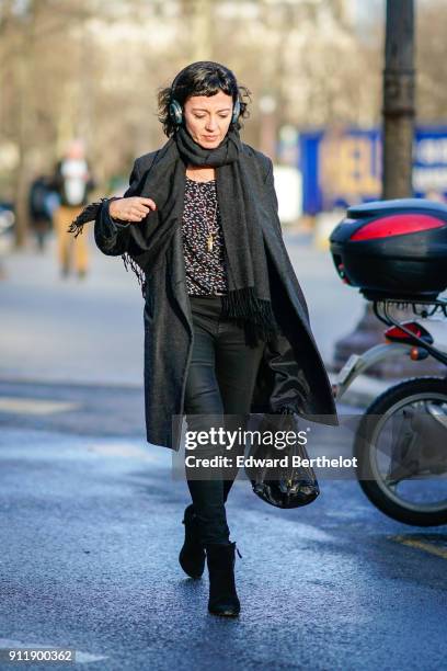Guest wears headphones, a scarf, a black jacket, black pants, a black leather bag, outside Chanel, during Paris Fashion Week -Haute Couture...