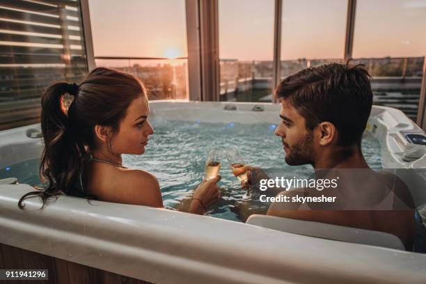 jong romantische koppel roosteren met champagne in een jacuzzi. - bathing in sunset stockfoto's en -beelden