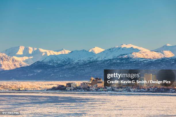 view of downtown anchorage in winter and the snow-capped chugach mountains beyond seen from point mackenzie, the skies in the background clear and bright, sea ice covering cook inlet in the foreground, south-central alaska - アンカレッジ ストックフォトと画像