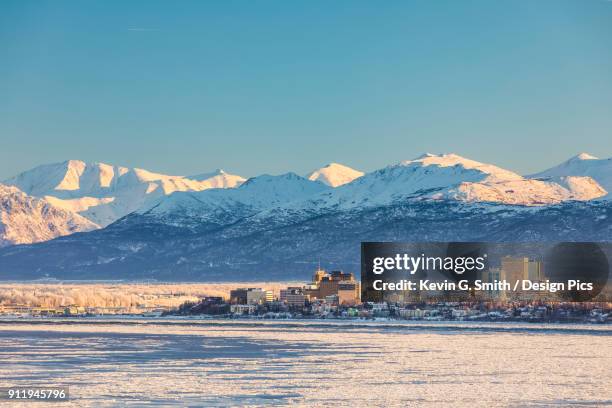 view of downtown anchorage in winter and the snow-capped chugach mountains beyond seen from point mackenzie, the skies in the background clear and bright, sea ice covering cook inlet in the foreground, south-central alaska - anchorage alaska stock pictures, royalty-free photos & images