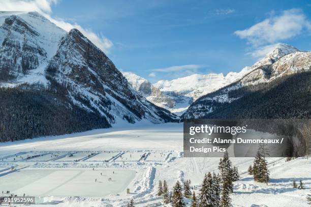 a wide angle view of lake louise from the upper floor of chateau lake louise resort in the winter surrounded by snow capped mountains and filled with skaters on the ice rinks carved into the frozen lake - chateau lake louise stockfoto's en -beelden