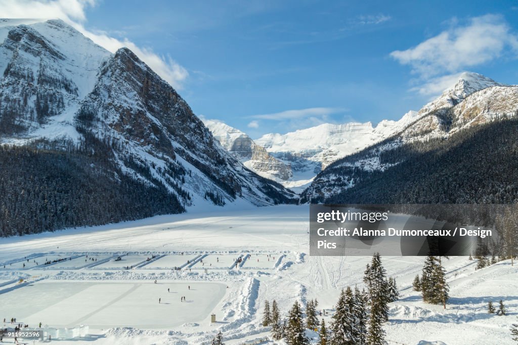 A Wide Angle View Of Lake Louise From The Upper Floor Of Chateau Lake Louise Resort In The Winter Surrounded By Snow Capped Mountains And Filled With Skaters On The Ice Rinks Carved Into The Frozen Lake