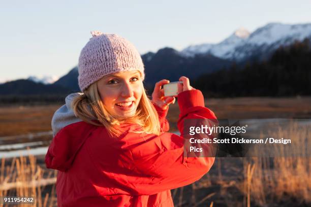 a young woman takes a picture of the kenai mountains in kachemak bay state park - kachemak bay stock pictures, royalty-free photos & images