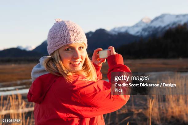 a young woman takes a picture of the kenai mountains in kachemak bay state park - kachemak bay - fotografias e filmes do acervo