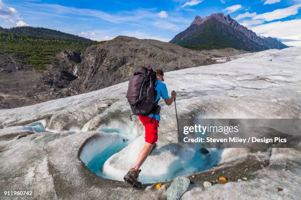 a backpacker crosses a stream on the surface of root glacier in wrangell-st. elias national park. donoho peak is in the background - root glacier stockfoto's en -beelden