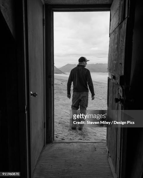a man and the valley of ten thousand smokes is framed by the doorway of one of the baked mountain huts in katmai national park - baked alaska stock-fotos und bilder