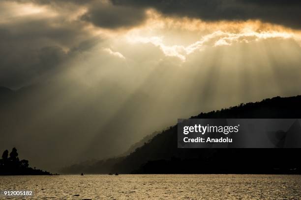 Group of cayucos sit in the mouth of a small bay as the sun set streams through the clouds over Lake Atitlan, Guatemala on January 22, 2018.