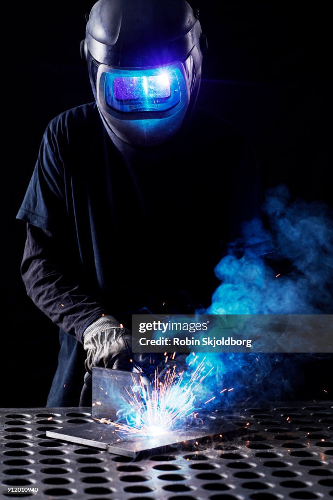 Blacksmith wearing protective mask welding in workshop