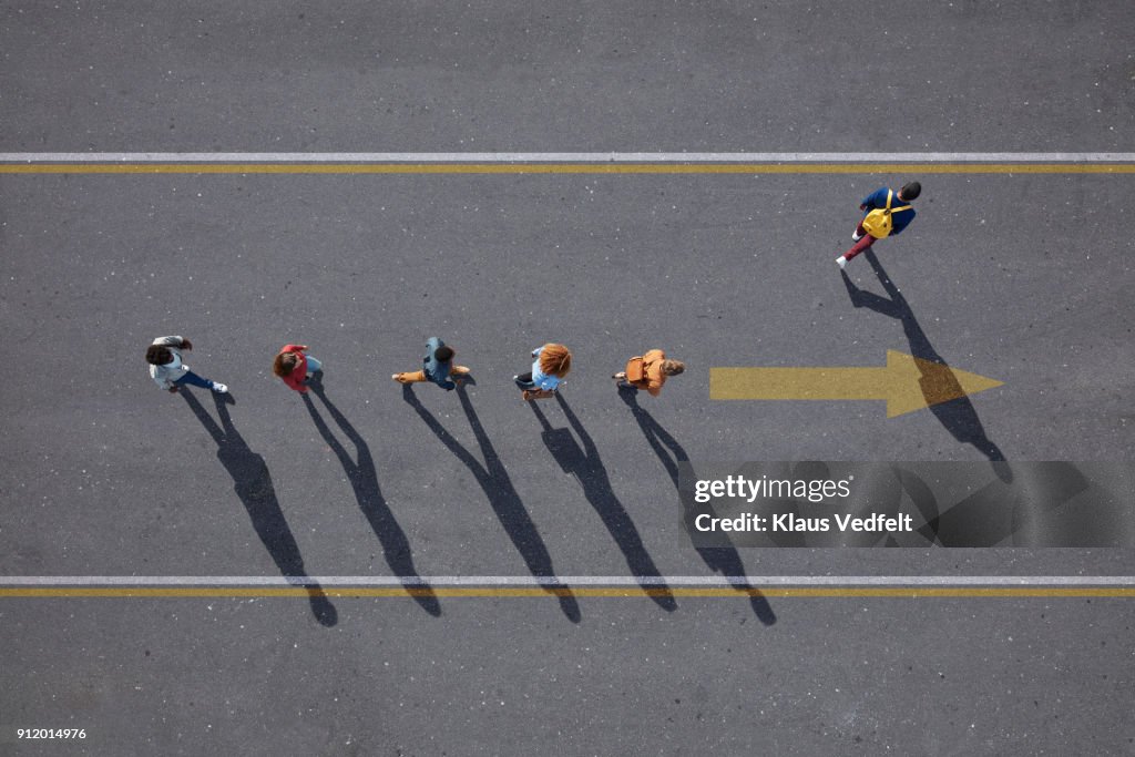 People walking in line on road, painted on asphalt, one person walking off.