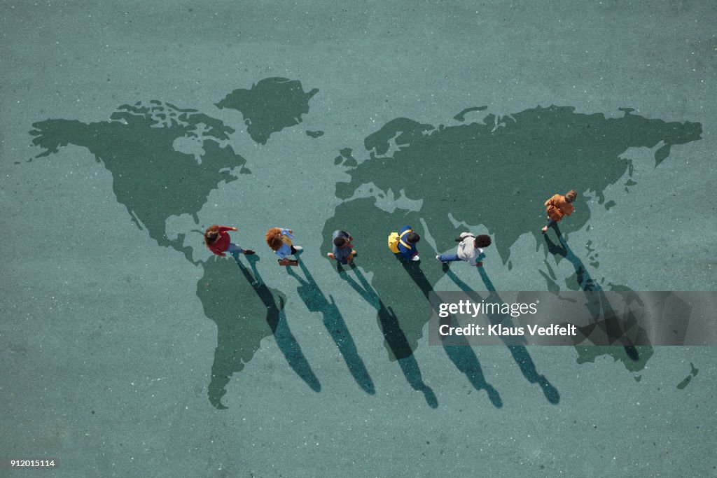 People walking in line across world map, painted on asphalt, front person walking left