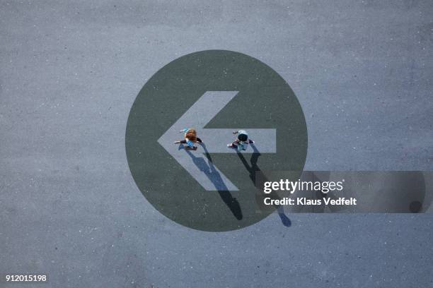 top view of two people walking across asphalt with big painted arrow - anführen stock-fotos und bilder