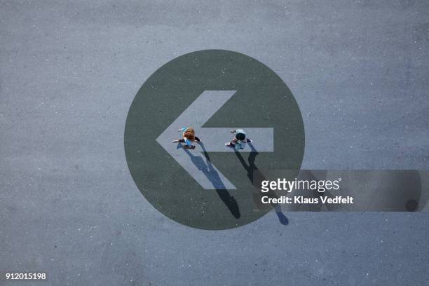 top view of two people walking across asphalt with big painted arrow - big dreams stockfoto's en -beelden