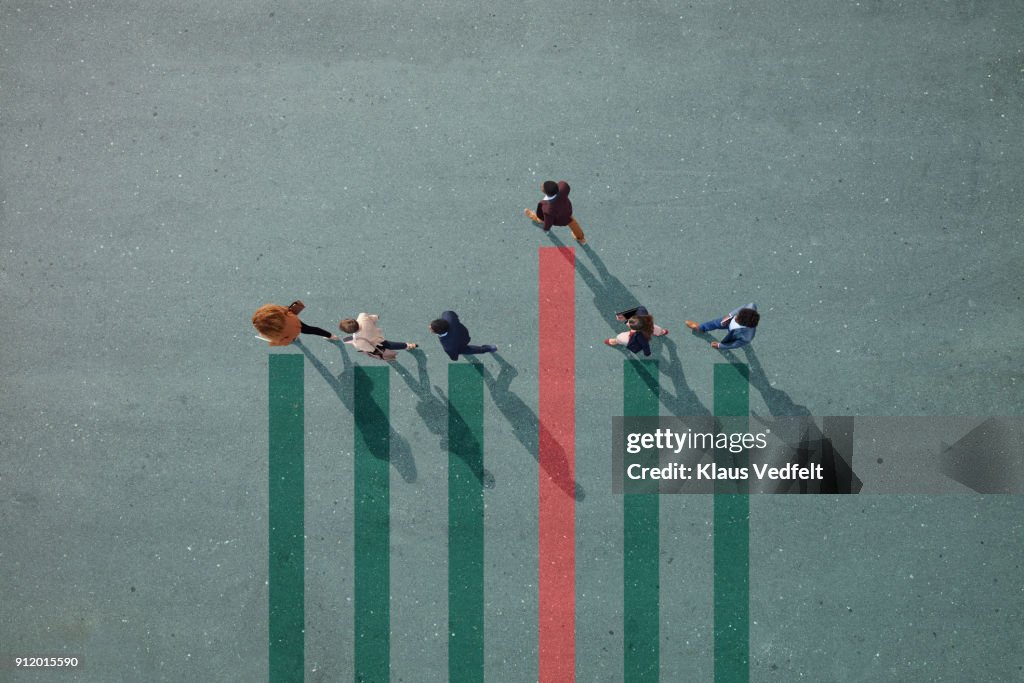 Businesspeople walking in line on bar chart painted on asphalt, one person walking off.