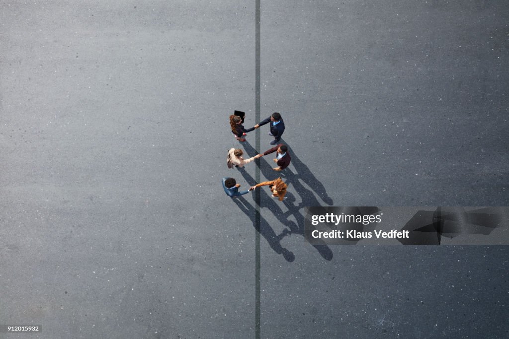 Businesspeople making handshakes across line, on painted asphalt