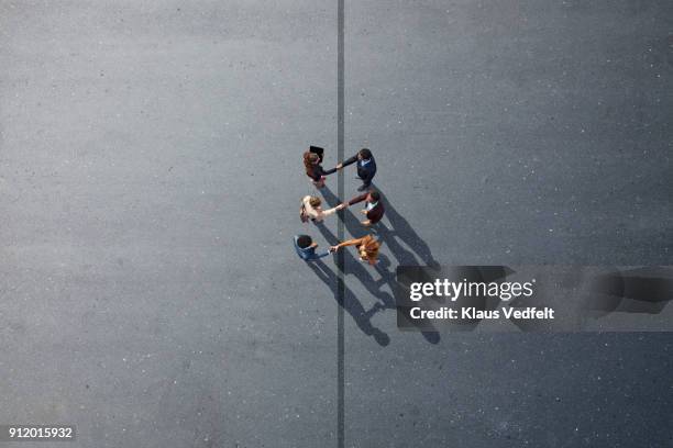 businesspeople making handshakes across line, on painted asphalt - business harmony stock pictures, royalty-free photos & images
