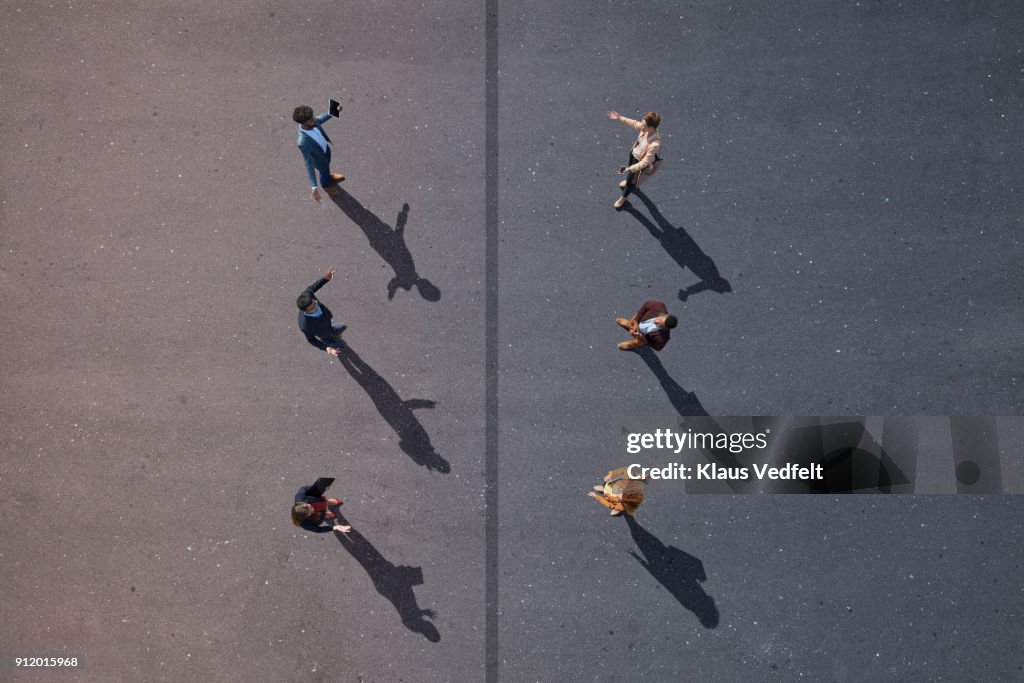 6 business people facing each other, with line dividing them, on painted asphalt