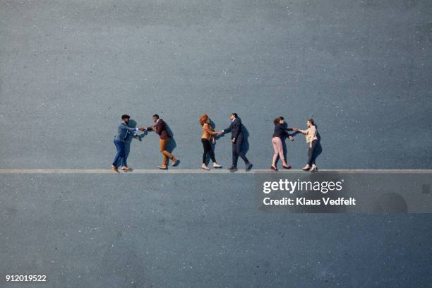 businesspeople lying down and shaking hands on line, painted on asphalt - encouragement stock pictures, royalty-free photos & images