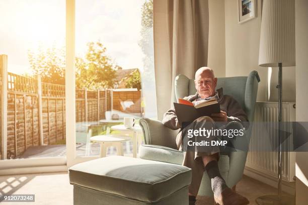 mature man sitting on arm chair and reading a book - reading imagens e fotografias de stock