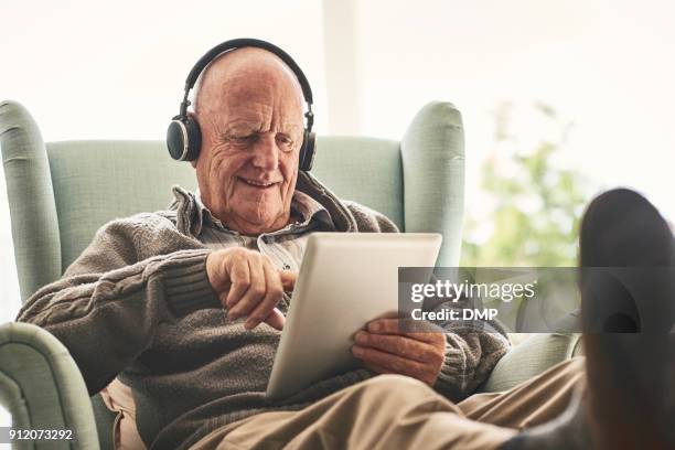 gelukkig bejaarde man thuis met behulp van digitale tablet - aging happy stockfoto's en -beelden