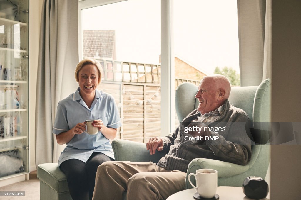 Senior hombre y cuidador hembra disfrutando de café en casa