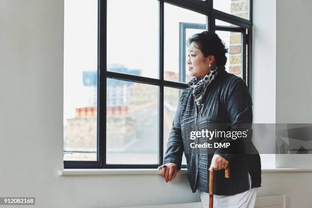 donna anziana con un bastone da passeggio che guarda fuori dalla finestra - bastone foto e immagini stock