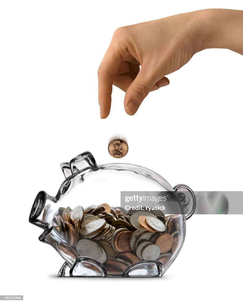 Female Hand Dropping Coin Into Clear Piggy Bank Isolated