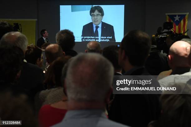 People watch on a screen a live broadcast of a speech by ousted Catalan separatist leader Carles Puigdemont at the New Year reception of the Leuven...