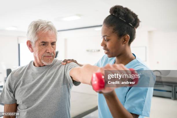 physiotherapist correcting her senior patient with his shoulder posture as he lifts free weights - man touching shoulder imagens e fotografias de stock