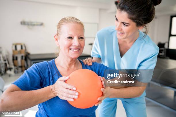 senior woman patient at physical recovery therapy exercising with a ball and therapist helping her - occupational therapy stock pictures, royalty-free photos & images