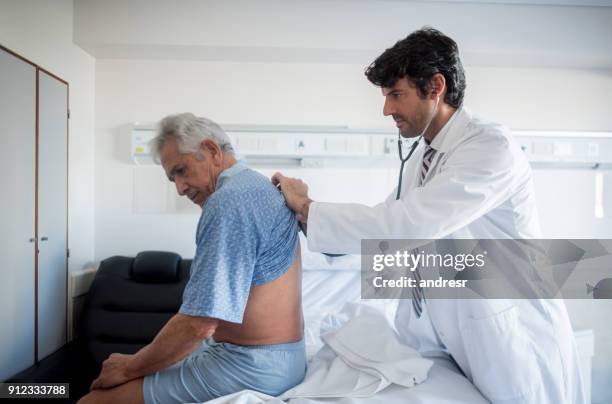 doctor haciendo sus rondas médicas en el hospital escuchando los pulmones de un pacientes - neumonía fotografías e imágenes de stock