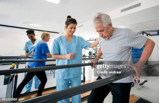 vielfältigen team von physiotherapeuten helfen patienten zwischen barren gehen - ergotherapie stock-fotos und bilder