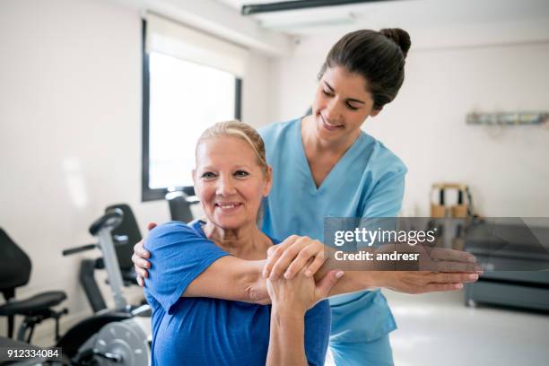 freundlichen physiotherapeuten holding senior patienten während sie ihre schulter streckt - man touching shoulder stock-fotos und bilder