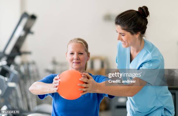 senior vrouw op fysieke rehabilitatie doen van een borst training en de therapeut helpt haar - ergotherapie stockfoto's en -beelden